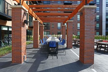 Courtyard of Oxbo Urban Rentals featuring a large dining table covered by a pergola near the grilling stations.